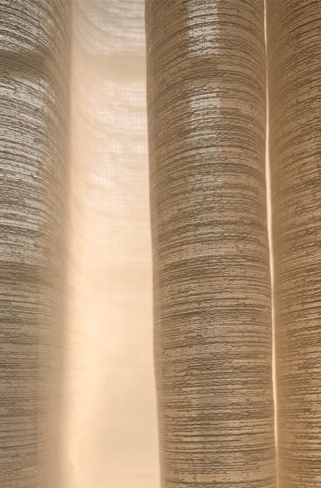 A close up of a set of white curtains with a light shining on them. The curtains are long and have a slightly fuzzy appearance, giving the impression of a soft, cozy atmosphere